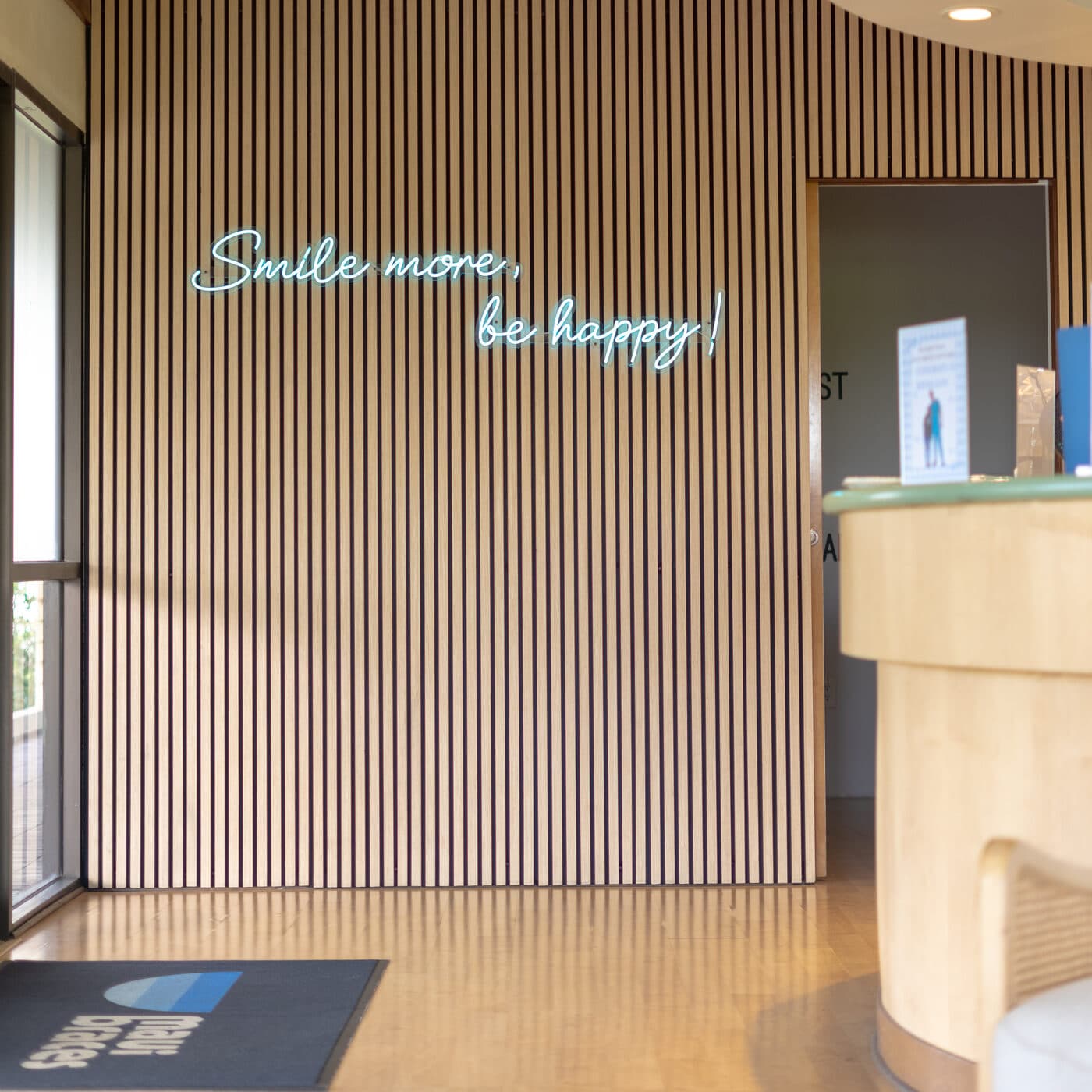 Reception desk and “Smile more, be happy!” neon sign at the Maui Braces Kahului office